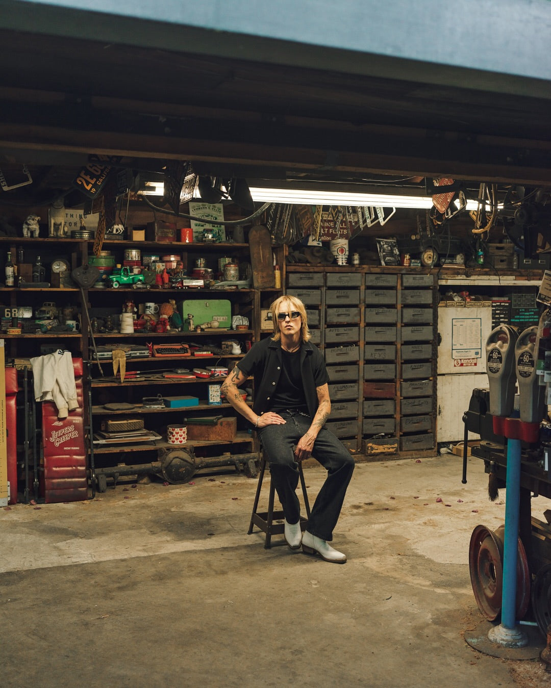 Person sitting on a stool in a workshop or garage filled with tools and equipment.