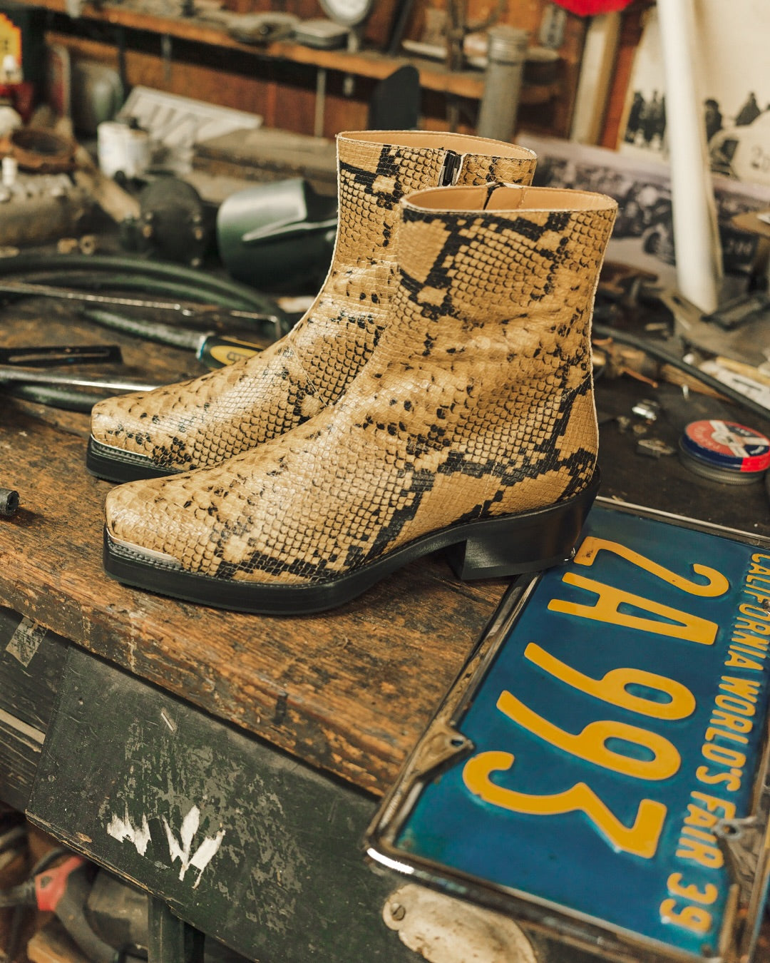 Patterned boots on a rustic workbench with tools and a vintage license plate.