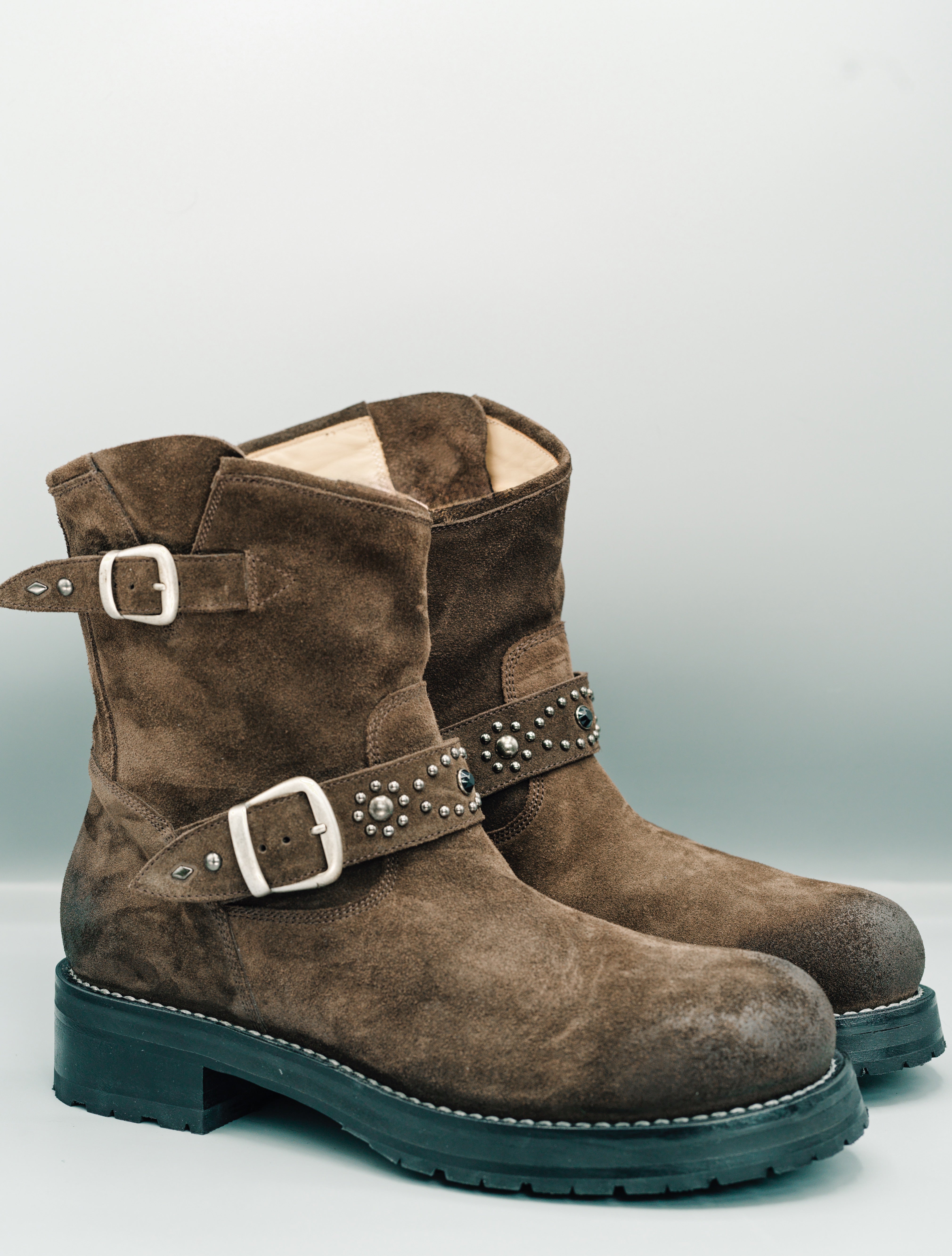 Pair of brown suede boots with buckles on a light gray background